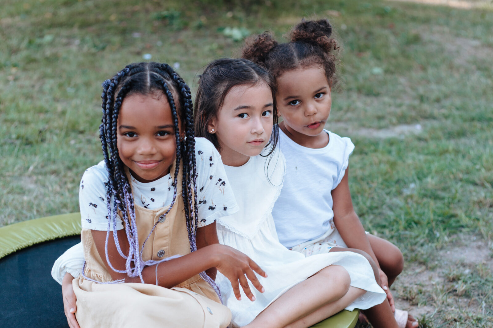 three multiracial children sitting outside on a trampoline
